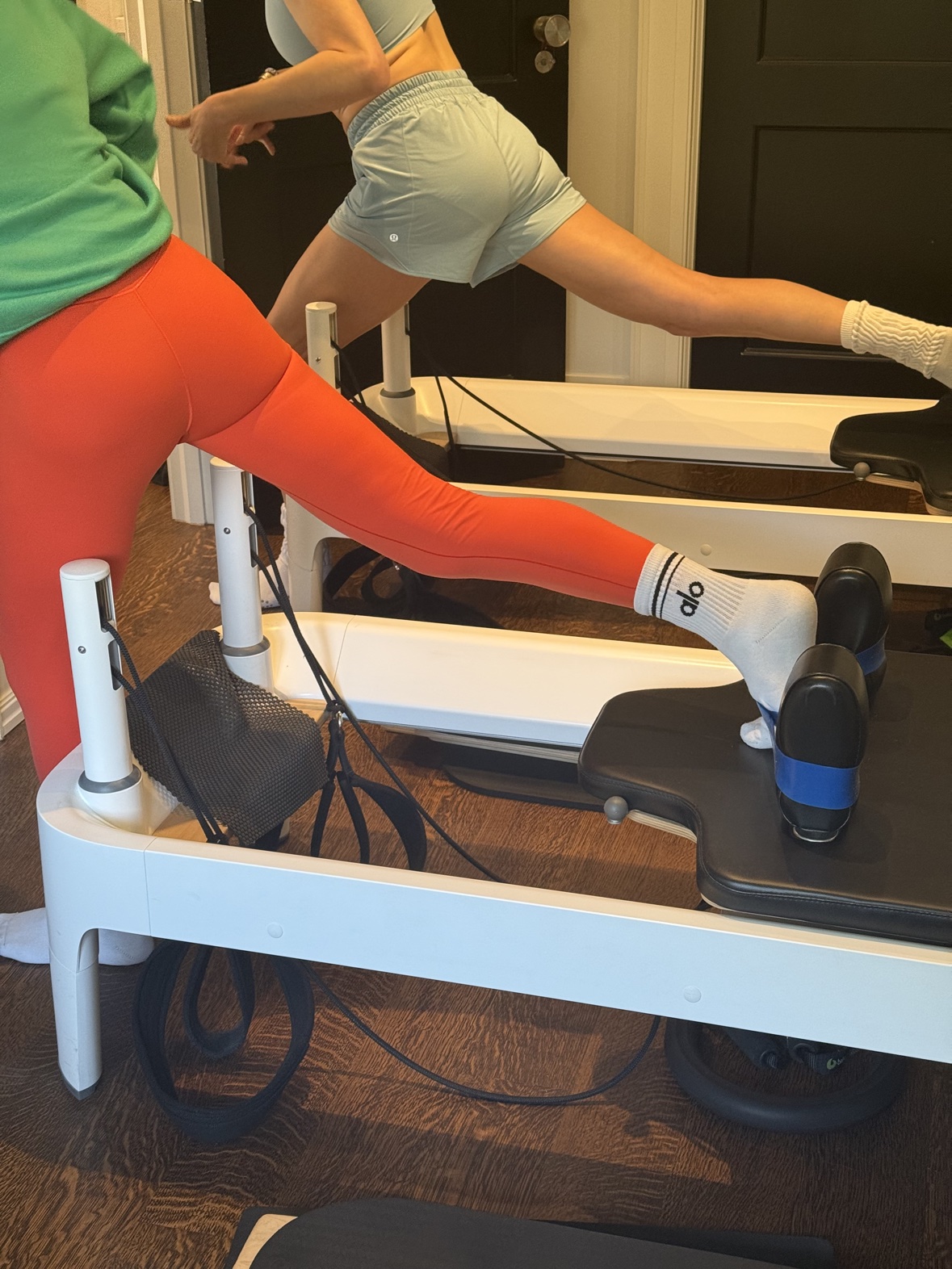 Two women extending one leg during a reformer Pilates exercise